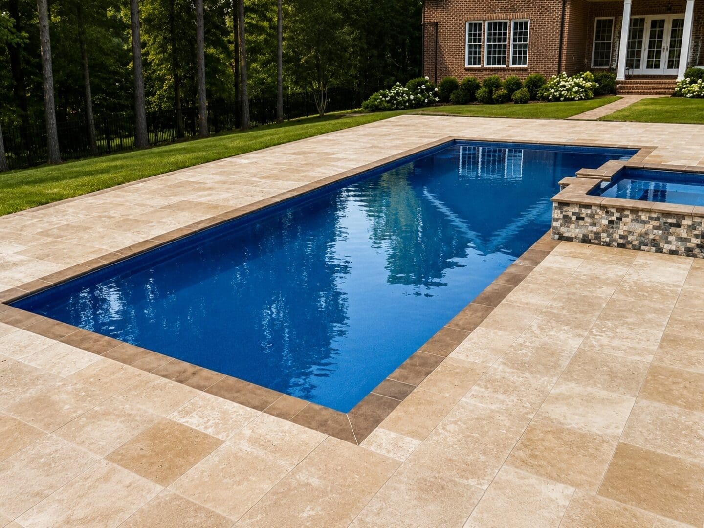 Completed rectangular fiberglass pool with raised spa and stone patio by B&B Decks and Pools.